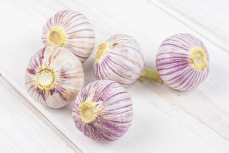 Group of five whole fresh purple single clove garlic on white woodの写真素材