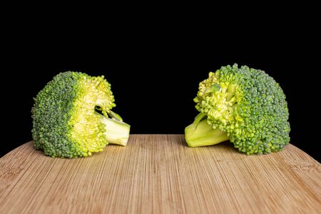 Group of two whole fresh green broccoli head on bamboo cutting board isolated on black glassの写真素材