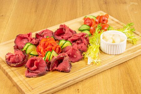 Beautiful sliced roast beef with pickled onions on wooden cutting board on lacquered wood