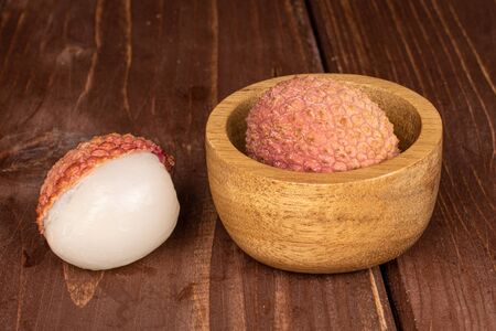 Group of two whole fresh lychee in bamboo bowl on brown woodの写真素材