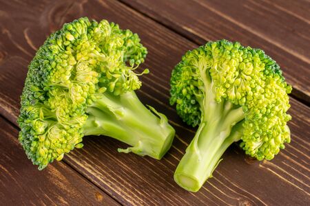 Group of two whole fresh green broccoli head on brown wood