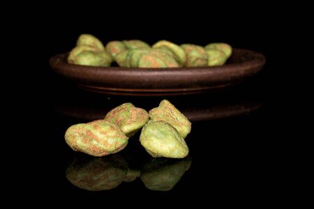 Lot of whole wasabi green peanut with brown ceramic coaster isolated on black glassの写真素材