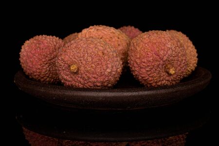 Group of seven whole fresh lychee with brown ceramic coaster isolated on black glassの写真素材