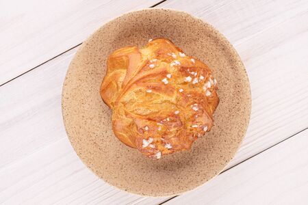 One whole fresh baked profiterole on ceramic plate on white wood