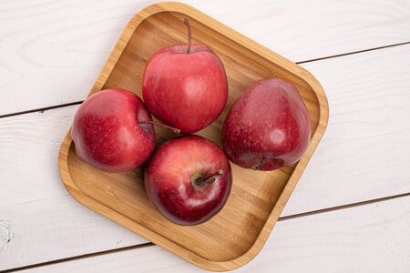 Group of four whole red delicious apple on wooden square plate on white woodの写真素材