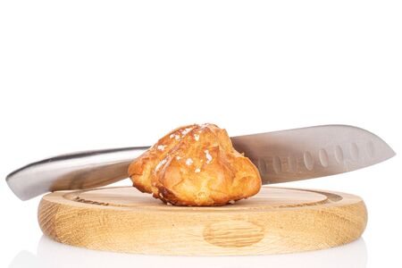 One whole fresh baked profiterole with knife on wooden plate isolated on white