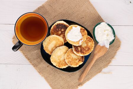 Group of six whole cheese pancake with cup of tea and sour cream on white wood