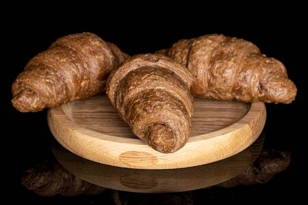 Group of three whole baked wholegrain croissant on wooden plate isolated on black glass