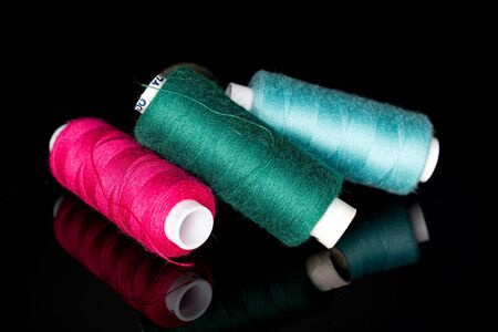 Group of three whole thread spools isolated on black glass