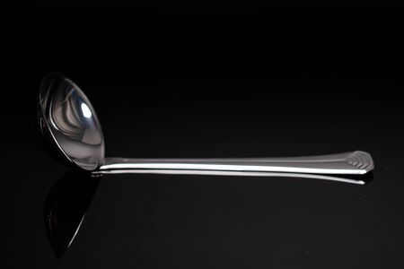 One whole steel silver ladle isolated on black glassの写真素材