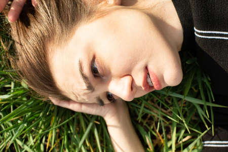Shiny lying portrait of white girl with dark eyes on green grassの写真素材