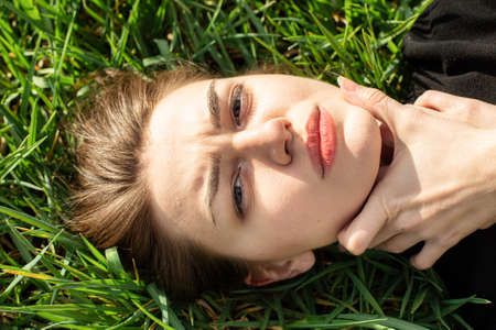 Lying choking portrait of white girl with dark eyes on green grassの写真素材