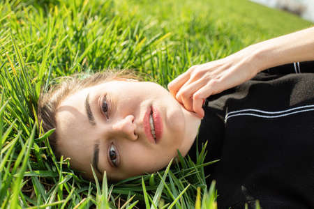 Lying portrait of white girl with dark eyes on green grassの写真素材