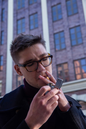 Smoking white european young man with city building behind with a lighter