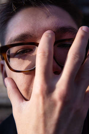 White european young man close-up portrait covered his face by handの写真素材