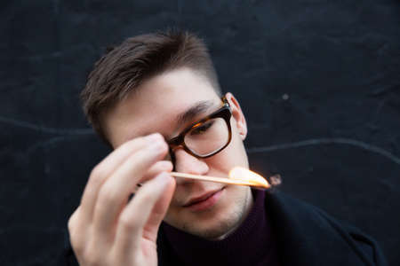 European young white man portrait isolated on black in glasses with burning matchの写真素材