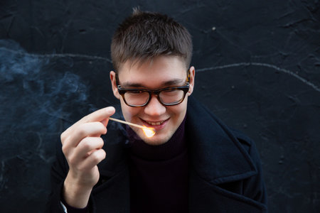 Smiling european young white man isolated on black with a burning matchの写真素材