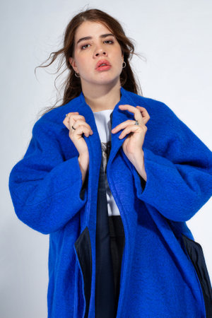Young european woman with brown hair on light grey in blue coatの写真素材
