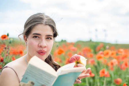 European young girl in summer poppy field with a book