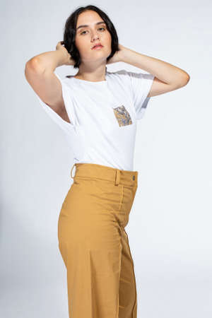 Young european woman standing in trousers on light grey with hands behind her headの写真素材