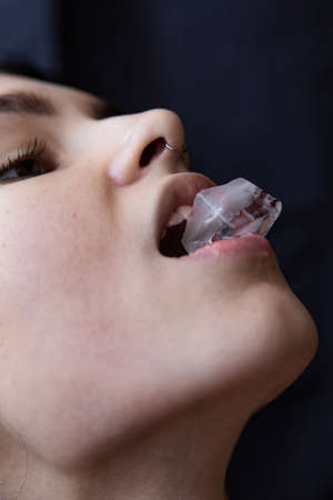 European woman with dark hair isolated on black with a piece of ice in the mouthの写真素材
