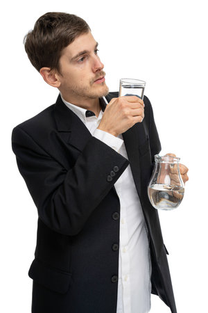 Young handsome tall slim white man with brown hair holding glass pitcher of water and glass of water isolated on white backgroundの写真素材
