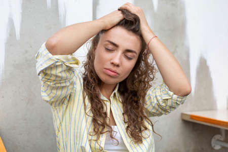 Young woman with long curly hair near the wall with closed eyesの写真素材