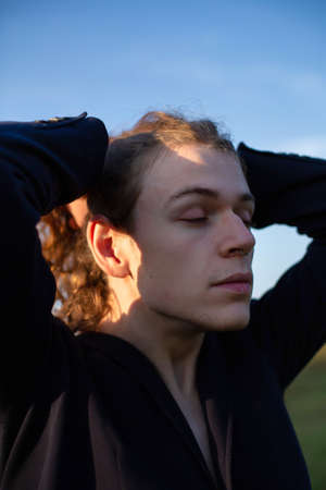 Young european white man with long hair with sky behind sunset lightの写真素材