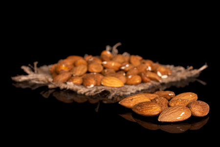 Lot of whole almond on natural sackcloth and few almonds aside in small group on black glassの写真素材