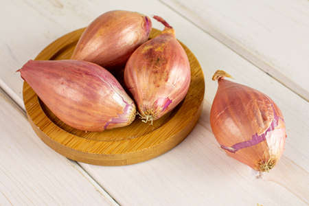 Group of four whole shallot on bamboo coaster on white woodの写真素材