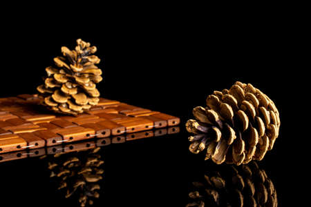 Group of two whole beautiful pine cone on bamboo coaster isolated on black glassの写真素材