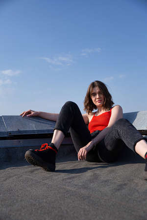Sitting young white european woman with dark hair on the roof with clear sky behind