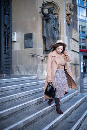 Pretty woman with curly hair on stairs of old building holding her hat because of the windの写真素材