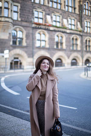 Pretty woman with curly hair in old town dressed in autumn coat and a hatの写真素材
