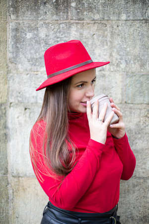Portrait of drinking white woman with long dark hair in bright red near stone wallの写真素材