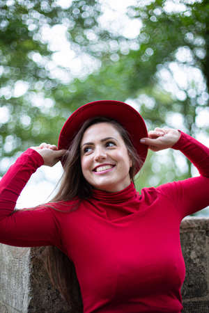Portrait of smiling white woman with long dark hair in bright red holding her hatの写真素材