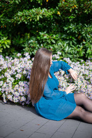 Sitting white young european woman near flowers in bright blueの写真素材