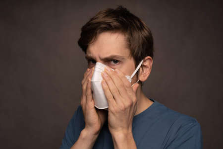 Young handsome tall slim white man with brown hair covering face mask with both hands in blue shirt...