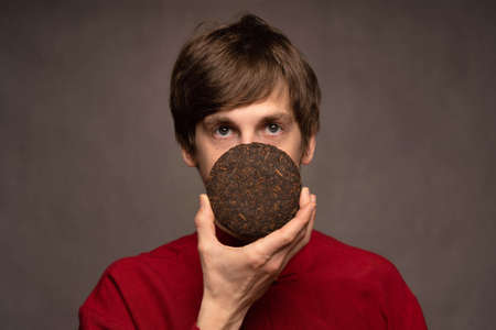 Young handsome tall slim white man with brown hair covering mouth with pu erh tea in red shirt on...