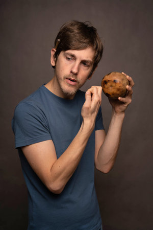 Young handsome tall slim white man with brown hair looking thoughtful holding mate cup in blue shirt...