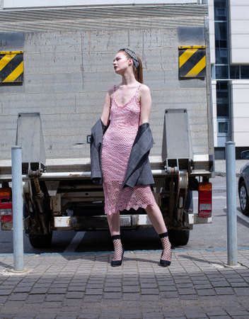 Pretty white blond young woman with a ponytail in pink summer dress with blue eyes in front of the lorryの写真素材