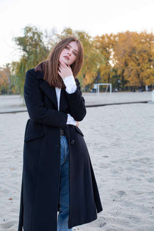 Long straight haired white european woman holding her chin in dark coat in autumn on the beachの写真素材