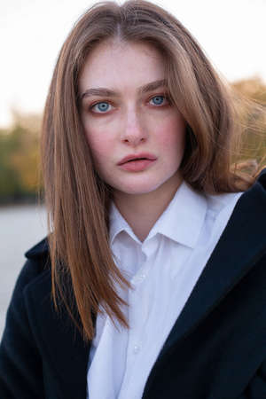 Portrait of attractive long straight haired white european woman in dark coat in autumn on the beach