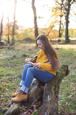 White young european woman in yellow sweater sitting on tree roots in sunny autumn forestの写真素材