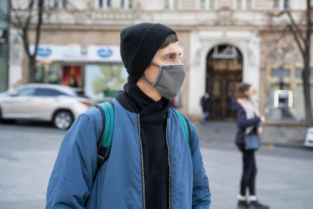 Young handsome white man with brown hair in blue jacket with black winter hat is looking sideways with the street scene in backgroundの写真素材