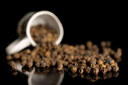 Lot of whole spicy black pepper in small ceramic cup isolated on black glass