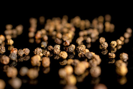 Lot of whole spicy black pepper isolated on black glass with small depth of fieldの写真素材