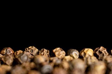 Lot of whole spicy black pepper on black background in closeup