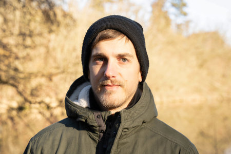 Young handsome white man with brown hair in dark green jacket has little smile on his face in the...