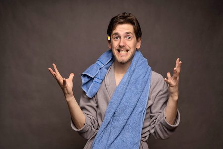 Young handsome tall slim white man with brown hair shining with excitement after shower in grey bathrobe on grey backgroundの写真素材
